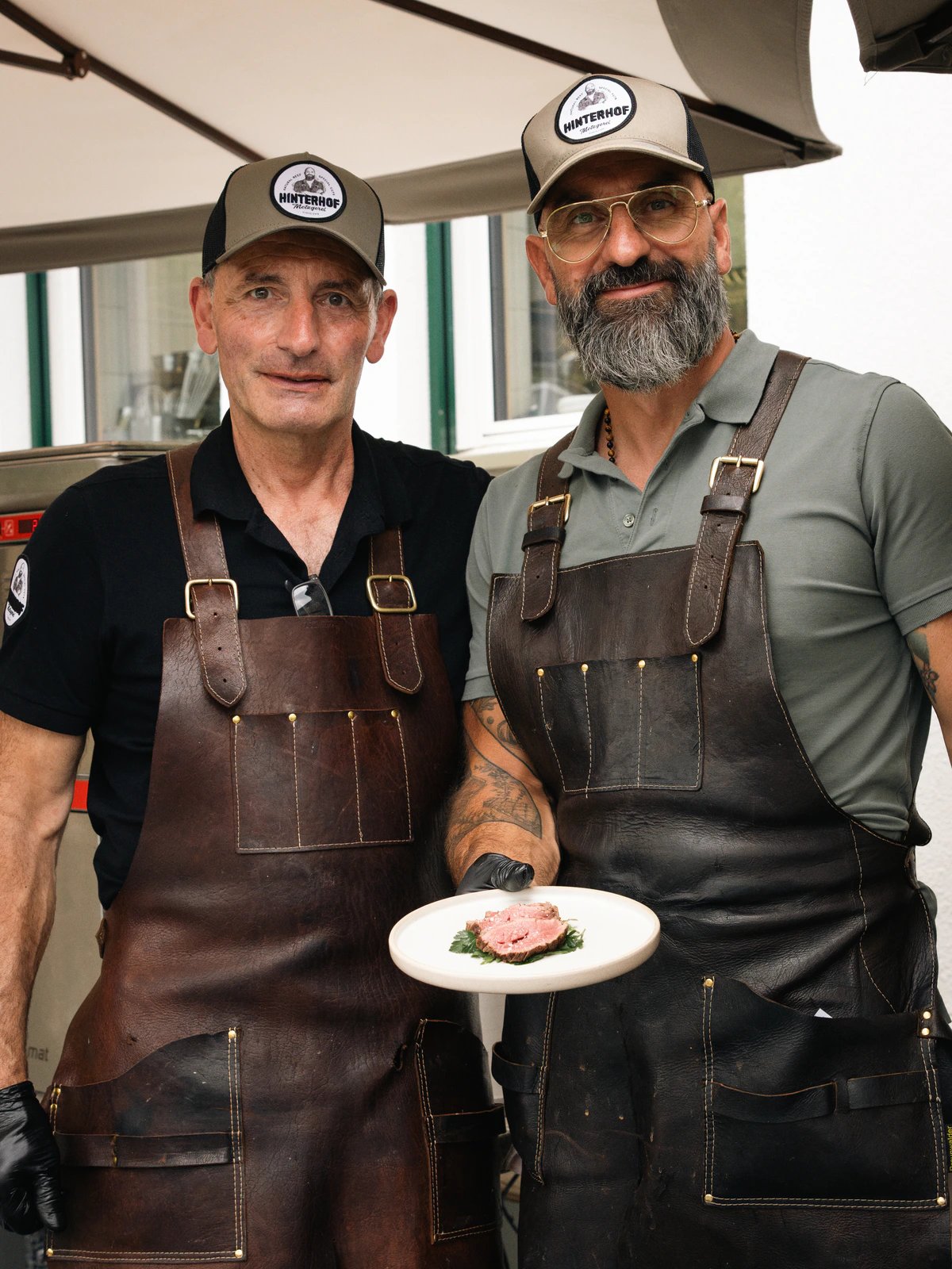 Two chefs in leather aprons presenting a plated dish.